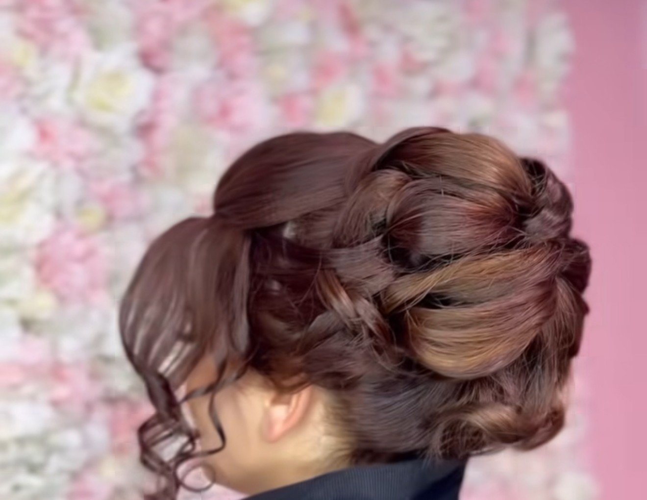 Opgestoken haar met krullen, voor een roze bloemenwand